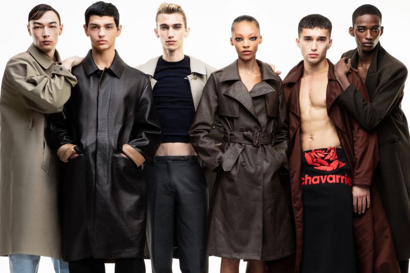 A diverse group of six fashion models wearing stylish trench coats and designer clothing pose in a studio against a white backdrop.