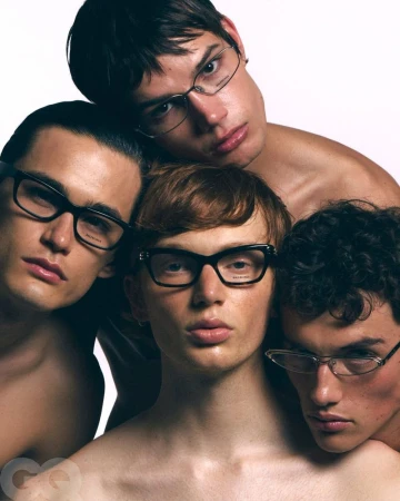 Group portrait of four adult male fashion models wearing eyeglasses posing together in a photo studio with a seamless white backdrop.
