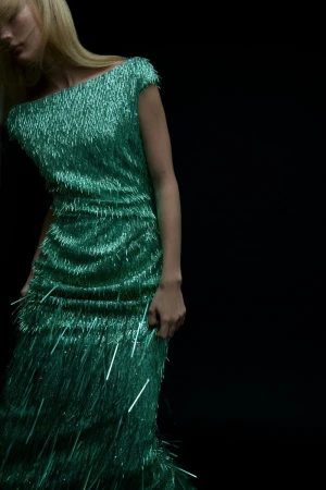 Woman in a shimmering green fringed evening gown against a dark backdrop, creating an elegant and eye-catching fashion moment.