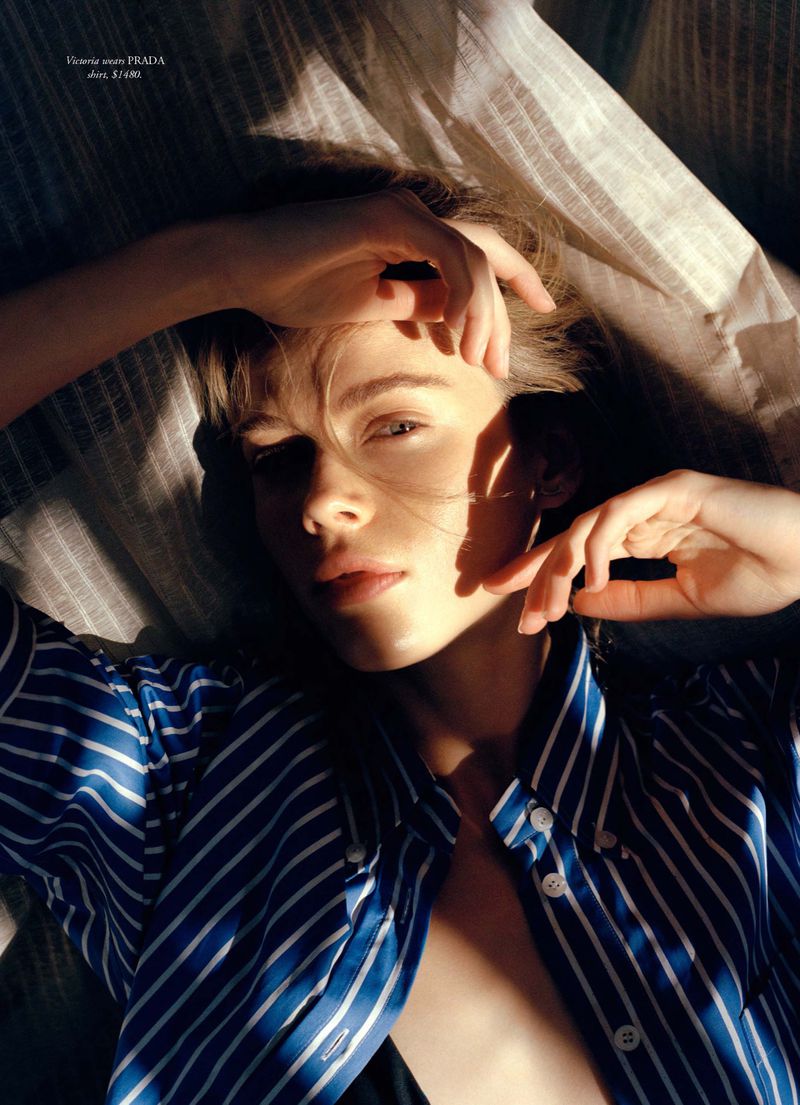 Close-up portrait of a young adult woman with blond hair, wearing a blue striped button-down shirt, lying on a striped surface.