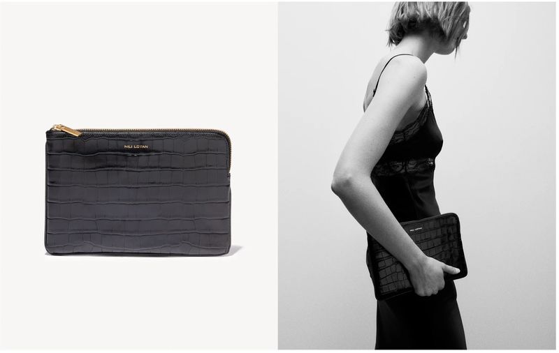 Black Nili Lotan clutch with gold zipper, embossed crocodile pattern, held by a woman wearing a black slip dress against a white backdrop.