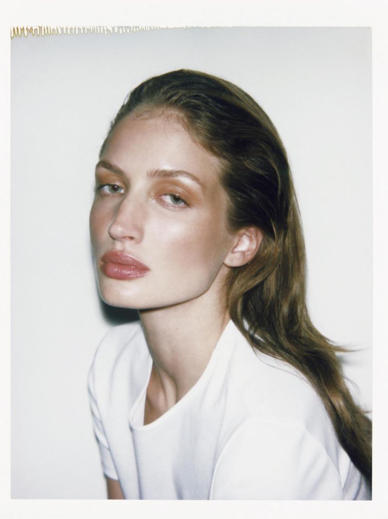 Close-up studio portrait of a fair-skinned adult woman with brown hair wearing a white t-shirt against a white background.