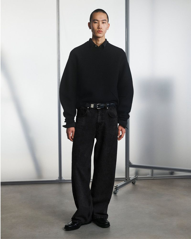 Full-length shot of an Asian male model posing in a black sweater and jeans against a neutral backdrop with metal frame.