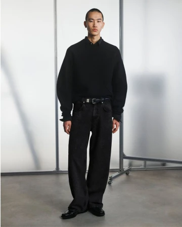 Full-length shot of an Asian male model posing in a black sweater and jeans against a neutral backdrop with metal frame.