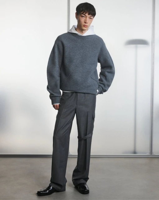 Studio shot of a young male model wearing a grey sweatshirt, pinstripe dress pants and black dress shoes, posing against a grey background.