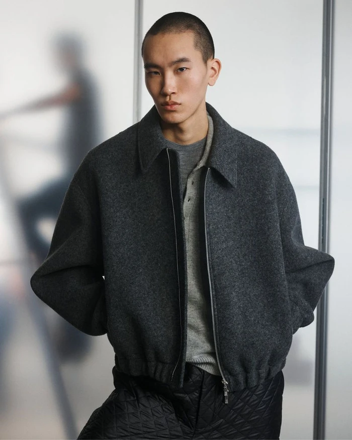 Close-up portrait of a male model wearing a dark grey wool jacket over a grey polo for Helmut Lang.