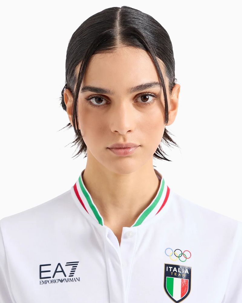 Close-up portrait of a young adult female with dark hair and fair skin, wearing a white collared shirt against a white background.