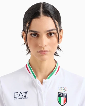 Close-up portrait of a young adult female with dark hair and fair skin, wearing a white collared shirt against a white background.