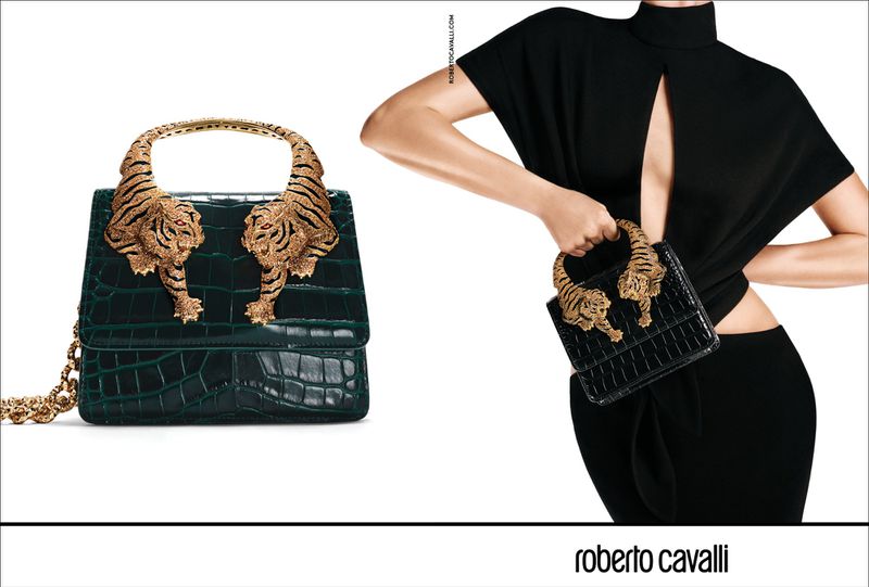 Crocodile-skin handbag with dual tiger-shaped handles in bronze, studio shot. A woman in black holds a smaller handbag with the same tiger detail.