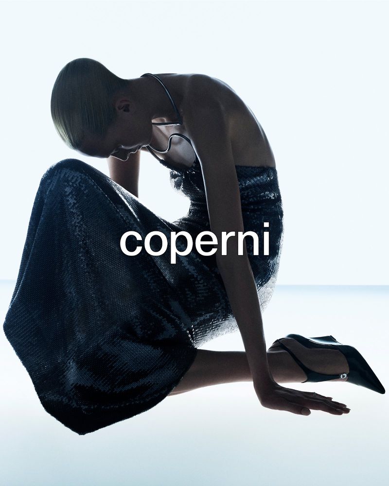 Alex Consani kneeling in a shimmering sequined halter gown and pointed slingback heels against a bright white backdrop for Coperni.