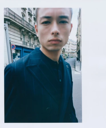 Portrait of an Asian man in a dark blue suit on a European city street with historical buildings in the background on an overcast day.