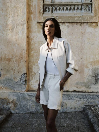 Model wearing an off-white zip jacket with matching shorts and a white top posing in front of a weathered stone building wall.