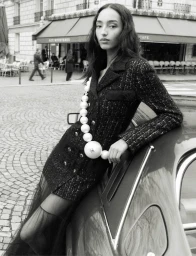 Model Mona Tougaard wearing a dark tweed jacket leaning against a car in front of a Paris cafe