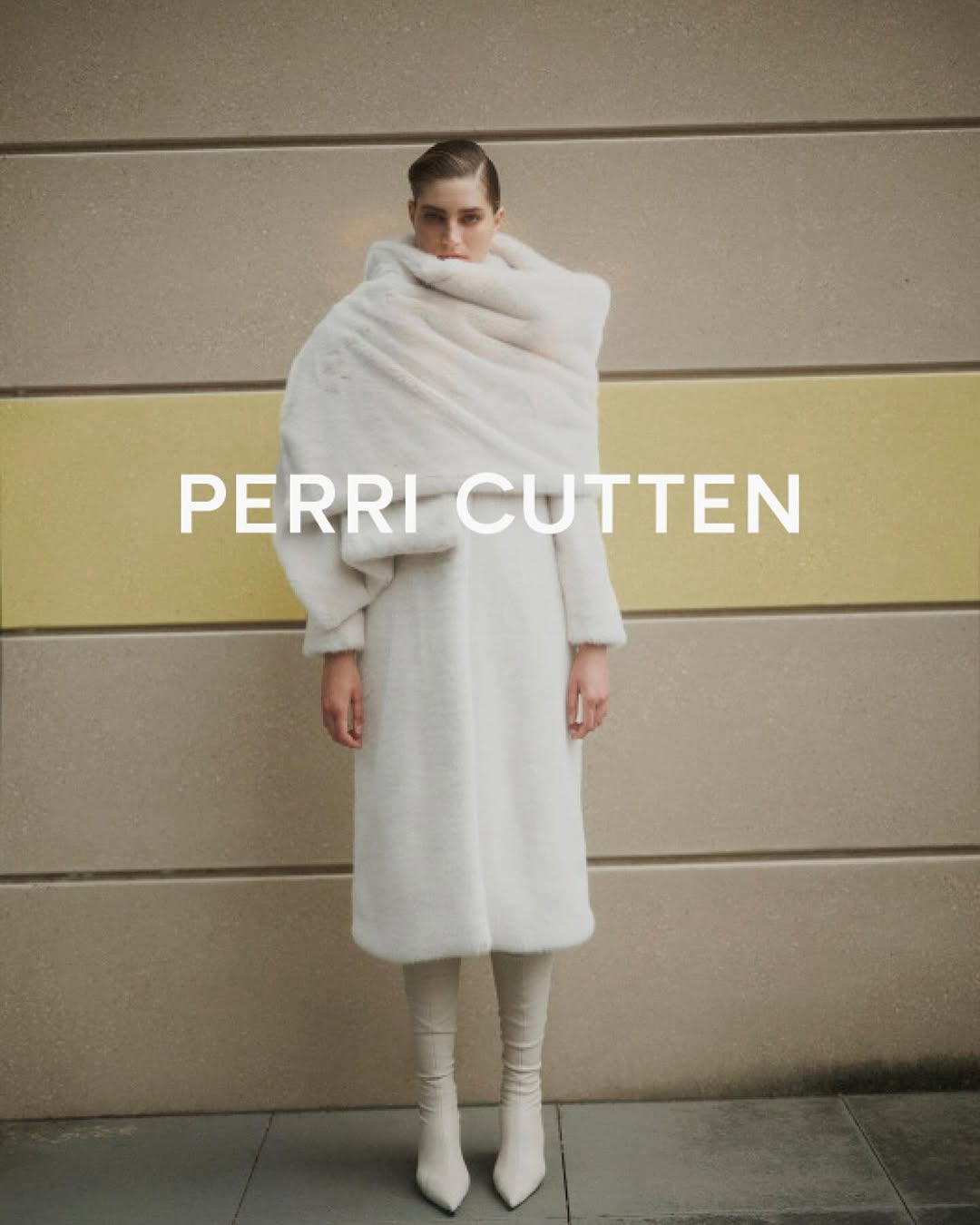 Fashion shot of a woman wearing a white coat and matching boots standing in front of a tan and yellow wall with the text PERRI CUTTEN.