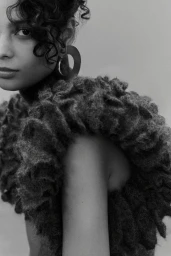 Close-up monochrome fashion portrait of a woman wearing a textured fuzzy garment and large hoop earrings against a neutral background.