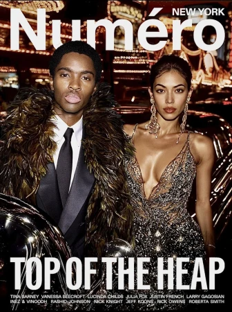 Magazine cover featuring a man in a feathered jacket and a woman in a beaded dress, set against a blurred city backdrop at night.