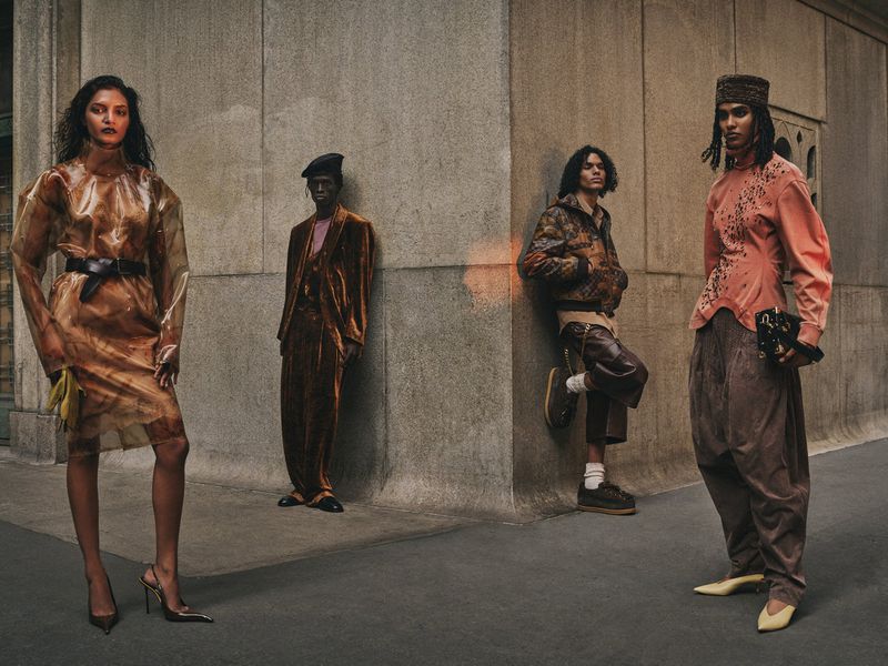 Editorial fashion shot featuring four diverse models in unique outfits against a concrete urban backdrop with natural, muted lighting.