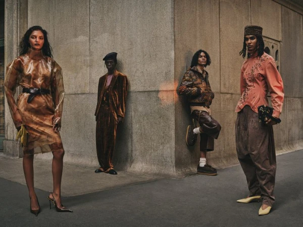 Editorial fashion shot featuring four diverse models in unique outfits against a concrete urban backdrop with natural, muted lighting.