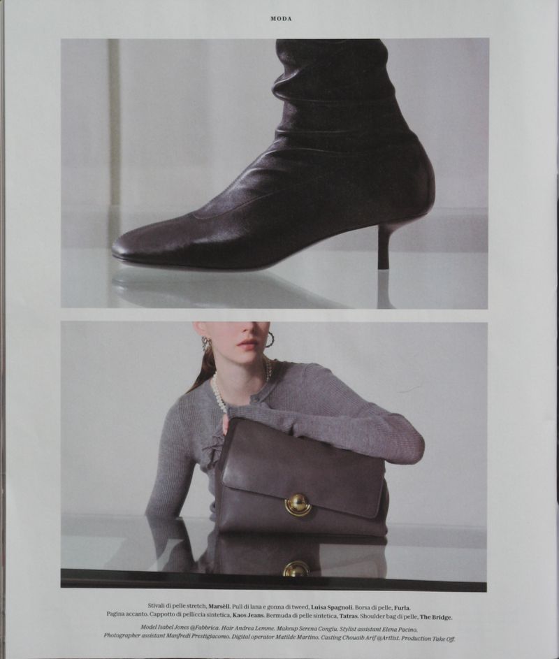 Fashion editorial featuring a woman in a grey outfit holding a brown handbag, paired with a high-heeled boot in a minimalist setting.