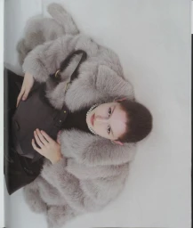 Overhead portrait of a woman wearing a fluffy grey fur coat and pearl necklace holding a dark bag