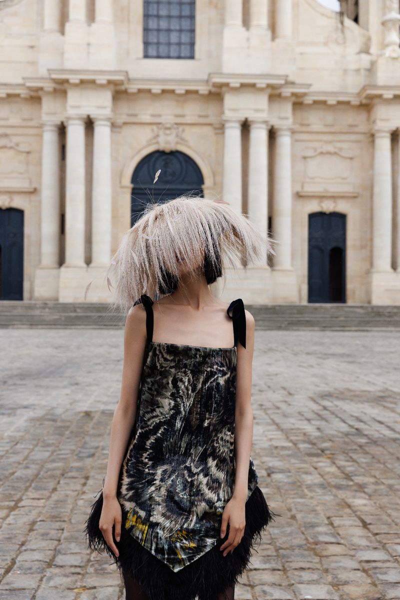 Woman in patterned dress with fringe standing in front of grand building with columns, on a sunny day. Fashion shot, architectural backdrop.