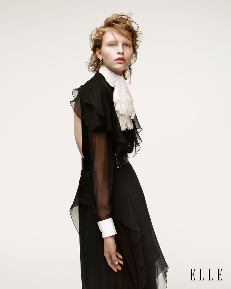 Fashion editorial portrait of a woman with red hair wearing a black ruffled dress with a white lace collar in a studio setting.