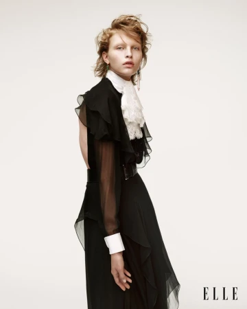 Fashion editorial portrait of a woman with red hair wearing a black ruffled dress with a white lace collar in a studio setting.