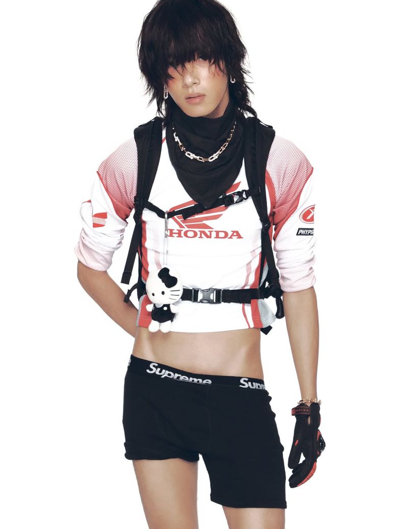 Androgynous person with dark hair poses indoors wearing a Honda crop top, black bandana, and black shorts with visible Supreme logo.