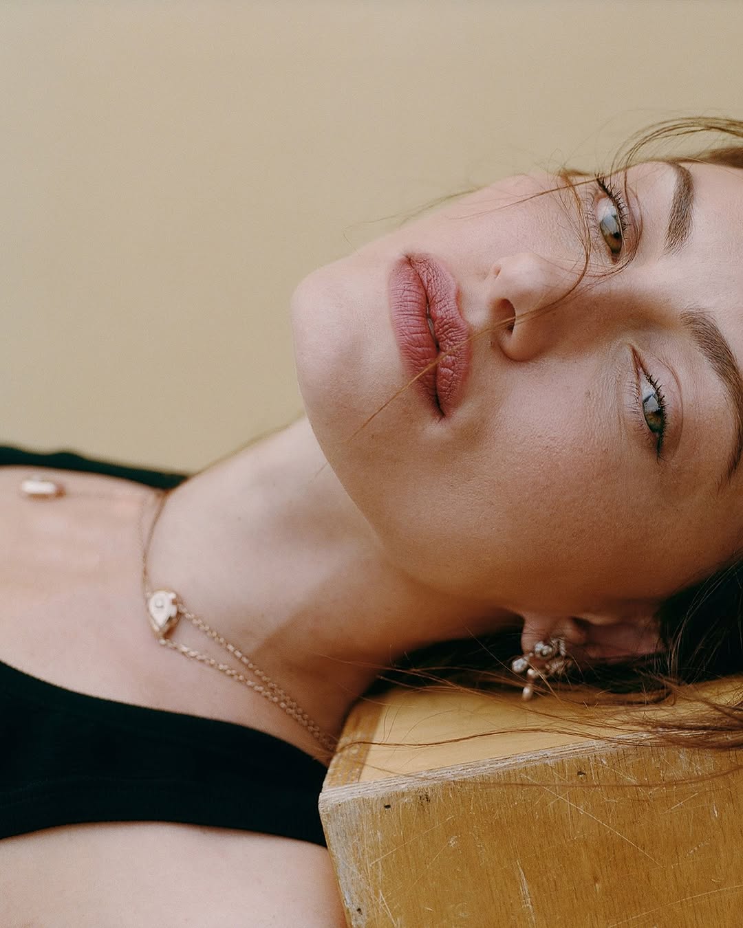 Woman with light skin and brunette hair lying on her side with a gold necklace and stud earrings in a close-up shot.