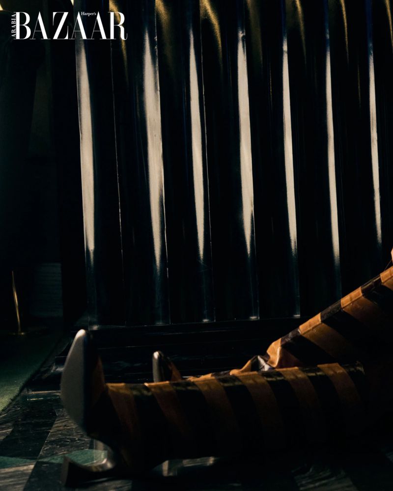 High-fashion editorial shot with dramatic lighting, featuring a black and yellow striped clothing piece against a dark, glossy background.