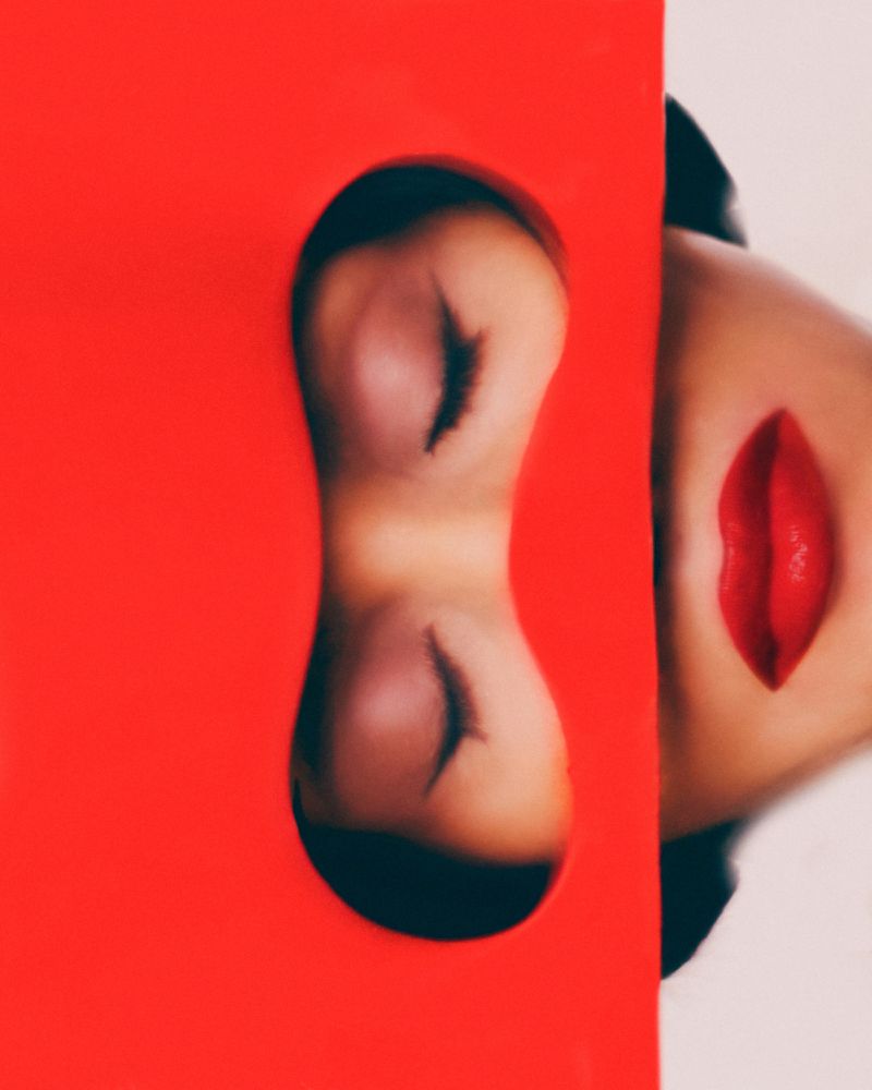 Close-up shot featuring a woman with a striking red lipstick, complemented by red color blocking and a distorted eye reflection.