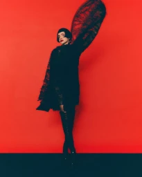Model Farida Khelfa wearing a black lace garment against a vibrant red background for Schön! Switzerland