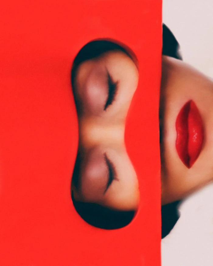 Close-up beauty portrait of Farida Khelfa with closed eyes and red lips framed through a bright red cutout mask.