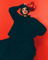 Model Farida Khelfa wearing a black outfit against a vibrant solid red studio background for Schön! Switzerland