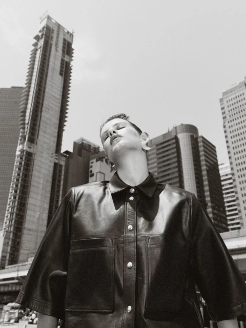 Monochrome portrait of a woman in a leather jacket against a backdrop of tall city buildings, showcasing urban fashion and style.