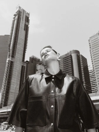 Monochrome portrait of a woman in a leather jacket against a backdrop of tall city buildings, showcasing urban fashion and style.