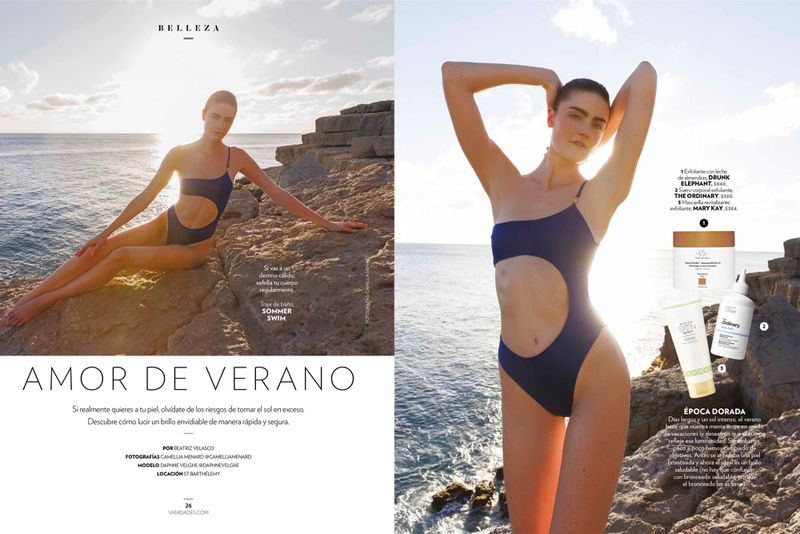 Fashion editorial shot of a female model in a blue one-piece swimsuit posing on rocky terrain overlooking the sea. Beauty and summer themed design.