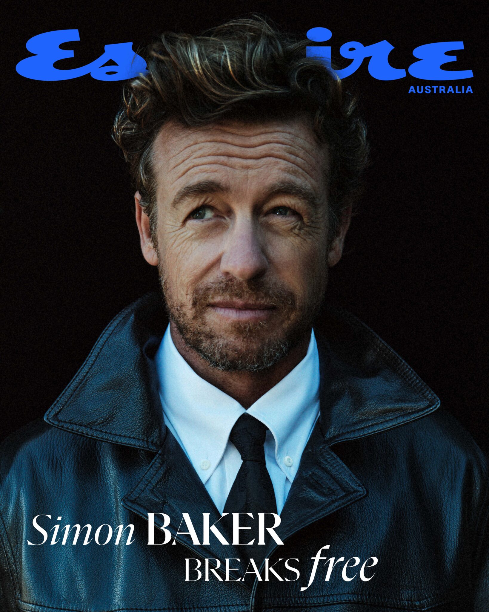 Close-up of Simon Baker on Esquire Australia cover, wearing a leather jacket, white shirt, and black tie, against a dark backdrop.