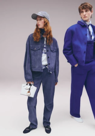 Two people model blue outfits and accessories in a studio setting, with one person holding a white handbag, showcased in a fashion editorial.
