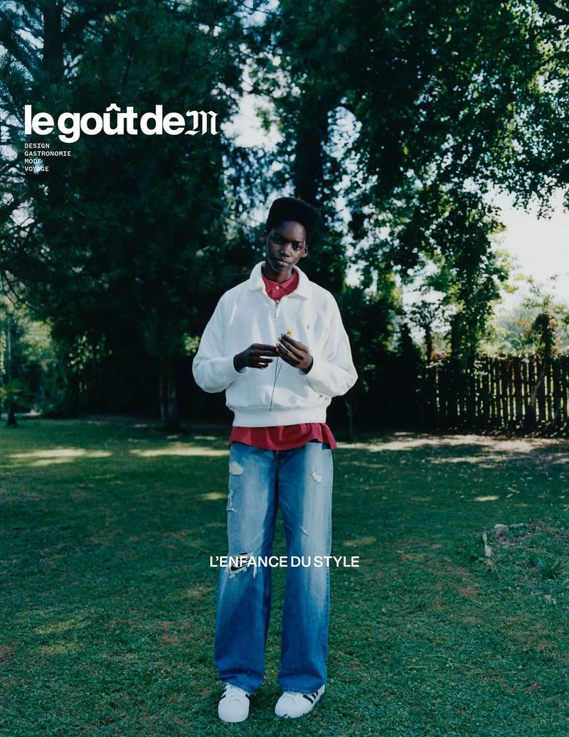 Magazine cover shot of a young adult standing on a lawn wearing a red shirt and oversized denim jeans in front of trees.