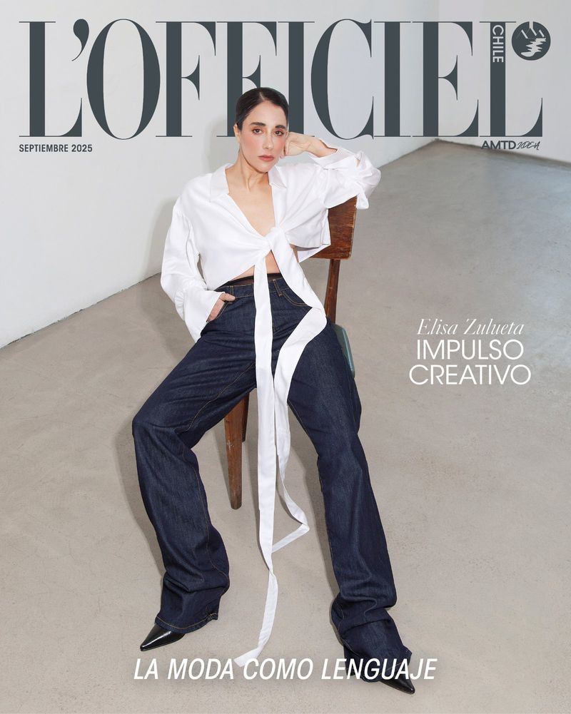 Magazine cover featuring a model wearing a white blouse and dark denim jeans, seated on a wooden chair against a neutral backdrop.