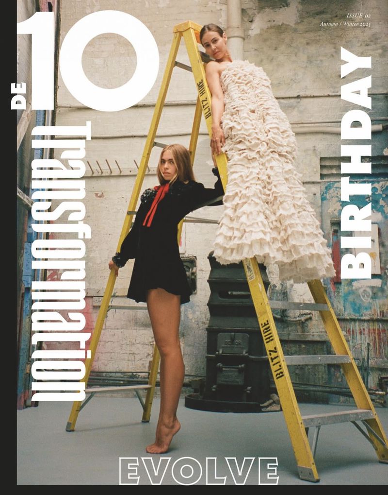 Fashion magazine cover featuring two women posing with a ladder, one in a black dress and the other in a white dress, indoor setting.