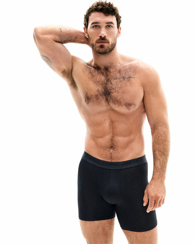 Athletic man in black boxer briefs poses against a bright white backdrop, highlighting his physique and the garment's fit and style.