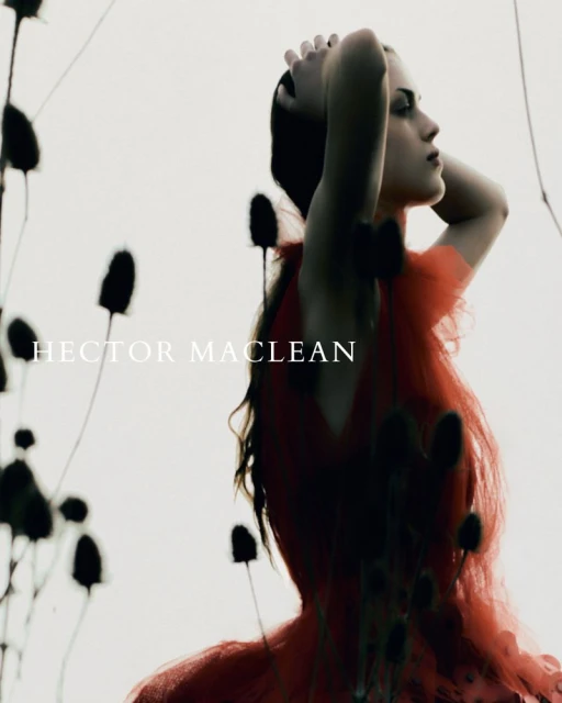 Woman in red dress stands in profile with hands on head among dark floral silhouettes on a white background in a fashion shot.