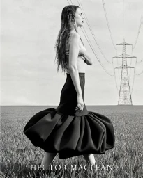 Monochrome portrait of a woman in a black sculptural bubble skirt walking in an open field with an electricity pylon in the background.