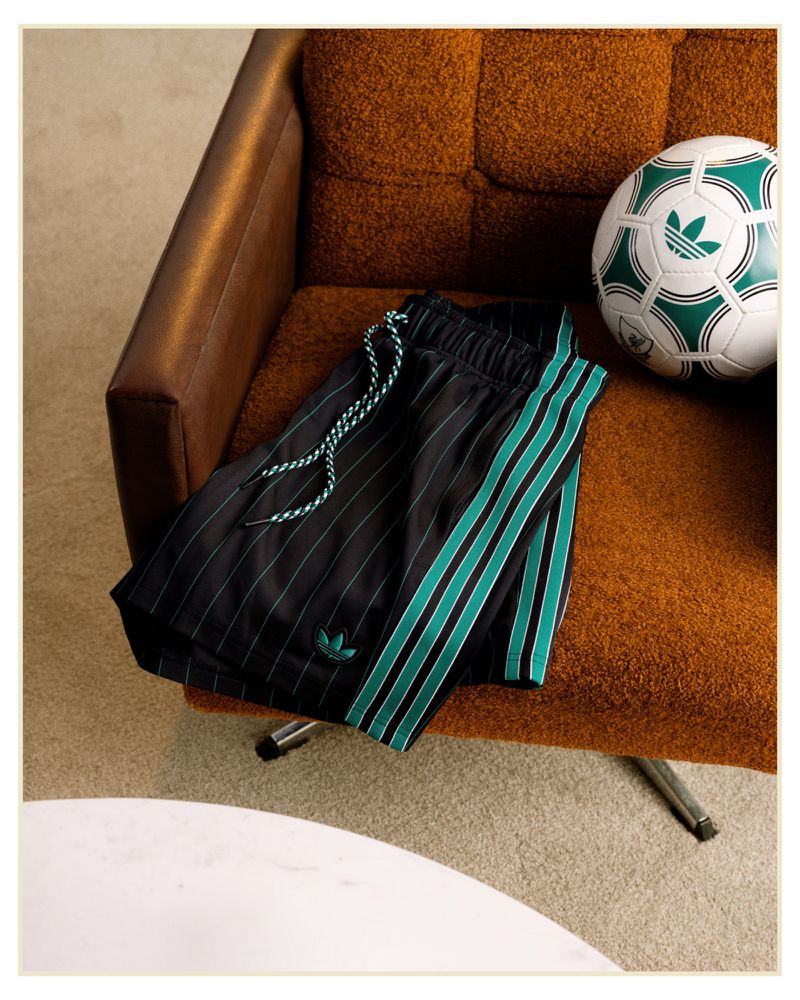 Studio shot of folded black Adidas track pants with green stripes and a soccer ball on an orange textured chair, creating a sporty vibe.