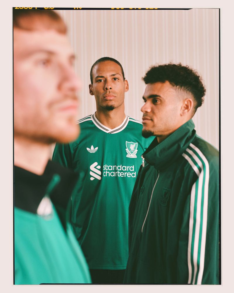 Three male soccer players in green vintage-style jerseys stand indoors for a sports-themed portrait; green, black, and white uniform details.