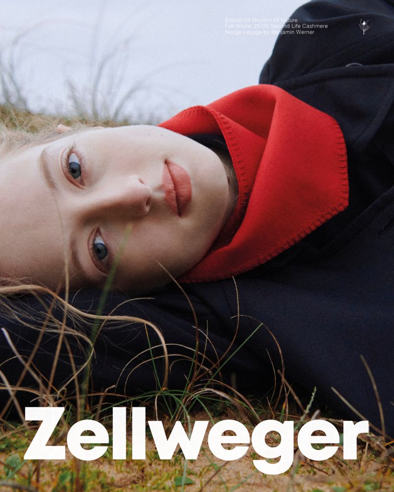 Close-up portrait of a blonde woman lying in grass, wearing a black coat with red collar and the text 'Zellweger' at the bottom.