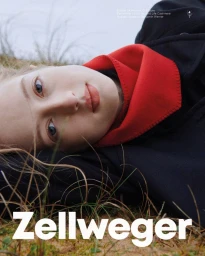 Model lying outdoors in grass wearing a dark coat and a bright red scarf for the Zellweger Warmwear Fall/W 25 campaign.