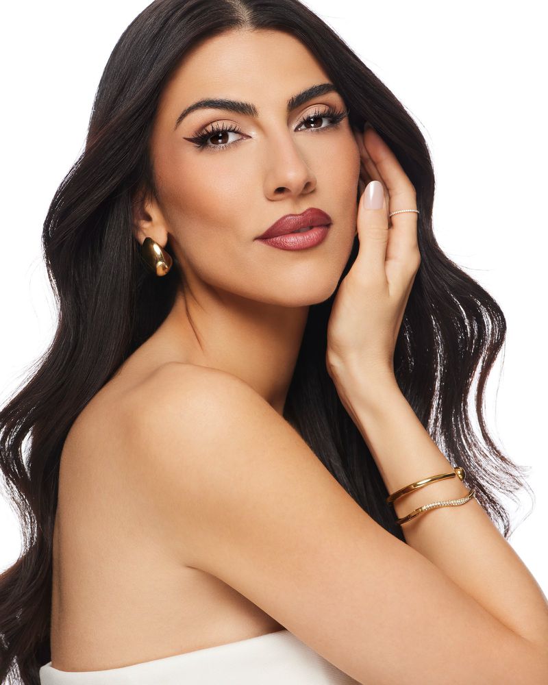 Portrait of an adult woman with long black hair, wearing jewelry and makeup, against a white background. Beauty and fashion shot.